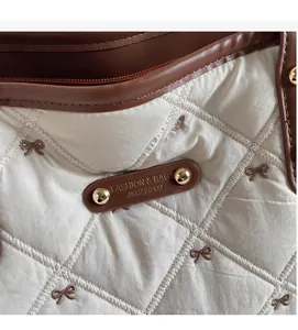 Makro-Detail der cremefarbenen Stepptasche mit braunem Schleifenstick und Lederetikett
