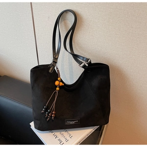 Détail du sac cabas en daim noir avec pampille orange et logo en métal brillant