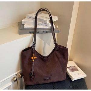 Gros plan détaillé du cabas en daim marron foncé avec pompon décoratif et écusson logo