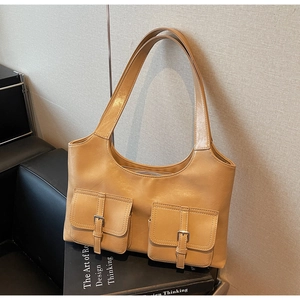 Close-up of khaki tote bag with front decorative pockets on a stack of design books