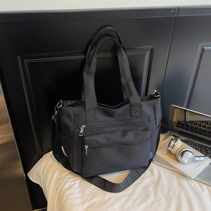 Detail of black nylon tote bag with dual front zipper pockets and adjustable wide strap
