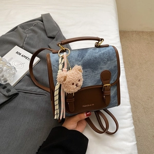 Détail du sac à dos en jean bleu avec garniture en cuir marron, boucles rétro et ourson