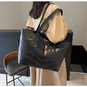 Detailed view of black quilted tote bag with white lettering on model's shoulder