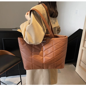 Detail of brown quilted tote bag with herringbone pattern and brand logo tag