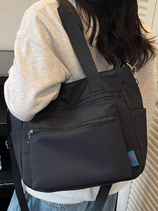 Large black nylon tote bag with multiple pockets worn over the shoulder by a model