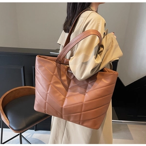 Detail of brown tote bag featuring V-shaped quilted texture and metal letter charm