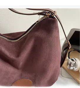 Detail of burgundy suede hobo bag featuring dark brown leather strap and gold zipper closure