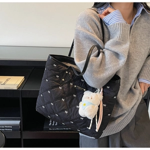 Detail der schwarzen Stepptasche mit weißen Schleifen und süßem Bärenanhänger