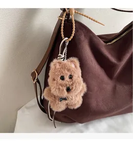 Detail of soft caramel plush bear charm with LOVE metal tag on a brown leather tote bag