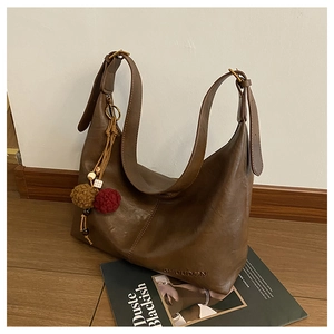 Detail of dark brown leather tote bag with pompom charm and embossed logo on magazine