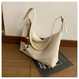 Detail of a creamy white half-moon shoulder bag with CHUUDON logo and pompom charm