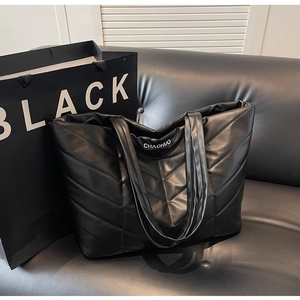 Detail of black chevron quilted tote bag with letter print on a leather sofa