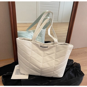 Macro detail of white quilted tote bag featuring V-shaped stitching and embroidered logo