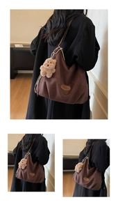 Detail of dark brown suede tote bag featuring a leather brand tag and plush bear charm
