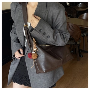 Close-up of a large dark brown leather tote bag featuring a decorative pompom and adjustable strap