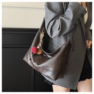 Detail of dark brown leather tote bag with logo and colorful plush ball charm accessories
