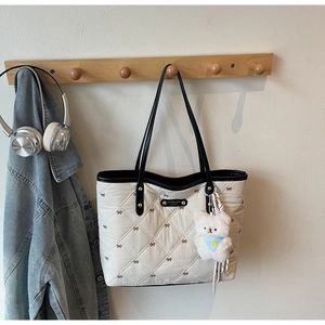 Detail der beigen Stepp-Tasche mit brauner Schleifenstickerei und schwarzen Ledergriffen