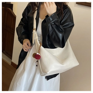 Detail of a minimalist off-white crescent tote bag with a double-color fur ball charm