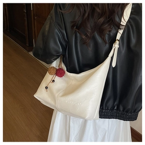 Detail of white leather tote bag with logo embossing and colorful plush pendant