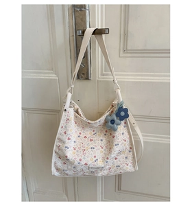 Close-up of floral tote bag with blue flower charms hanging on a white wooden door
