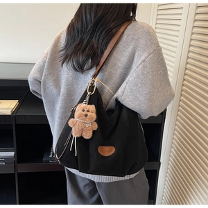 Close-up of black corduroy tote bag featuring a leather strap and a cute plush bear charm