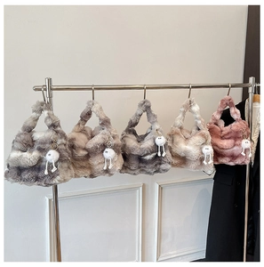 Row of colorful faux fur handbags with fluffy ball charms hanging on a metal rack