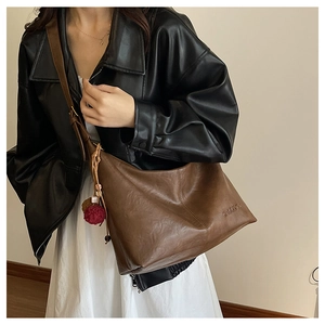 Close-up of the vintage brown leather tote bag with BHUUDCN logo and fuzzy red charm