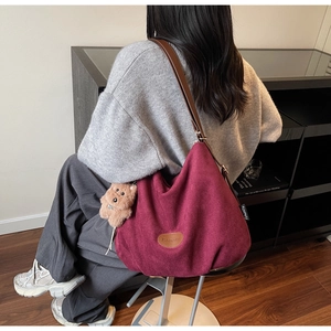 Detail of burgundy suede tote bag with leather straps and cute bear charm worn by a model