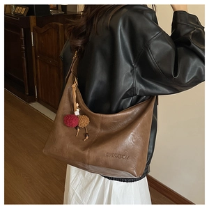 Detail of a brown leather tote with CHUUDON logo engraving and plush pom-pom charm