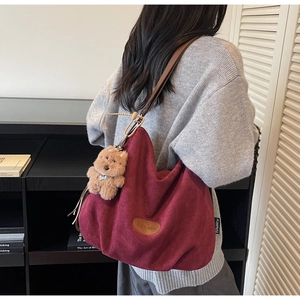 Detail view of burgundy tote bag with brown bear charm shown on a female model