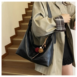 Detail showing the CHUI DON embossed logo on a black leather tote with fur ball charms