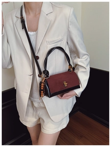 Detail view of burgundy wine handbag featuring a knotted rope handle and colorful wood beads
