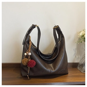 Detailed view of deep brown faux leather tote with logo embossing and plush pendant
