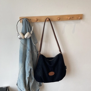 Detail of a black Hobo tote bag with brown leather strap and Banatu brand logo on white wall
