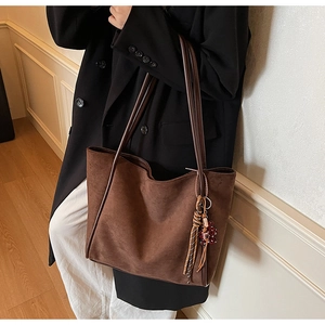 Detail of dark brown suede tote bag featuring a leather strap and woven tassel charm