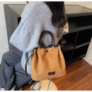 Détail du sac seau en daim camel avec fermeture à cordon et étiquette logo en cuir