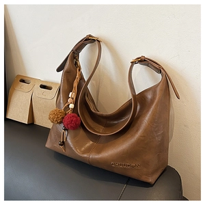 Detail showing vintage brown PU leather texture and steel-stamped logo with fur pom-pom charm