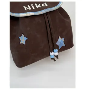 Detail of brown faux suede backpack featuring Nika embroidery and blue star patches