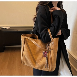 Brown suede tote bag with leather straps and heart charm detail on a model