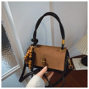 Detail view of vintage two-tone handbag featuring a gold twist lock and wooden bead charm