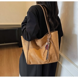 Detail of camel brown suede tote bag featuring a decorative polka dot tassel pendant
