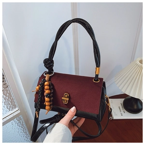 Detail of burgundy suede and black leather shoulder bag with golden lock and wood bead tassel
