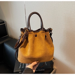 Détail d'un sac seau en daim jaune gingembre avec poignées en cuir et boucle décorative
