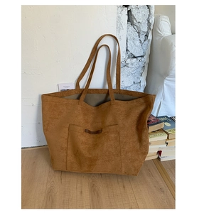 Détail d'un sac cabas en daim marron avec poche cousue et étiquette en cuir rustique