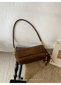 Detail of a brown suede shoulder bag with vintage tassel and gold metal hardware