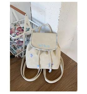 Detail of cream drawstring backpack with Nika embroidery and plaid star patches on wood