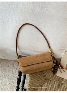 Detail of tan suede baguette bag with wooden beaded pendant on a woven surface