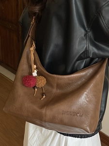 Brown vintage leather shoulder tote bag with plush charm on a black leather jacket