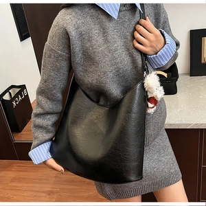 Gros plan d'un grand sac bandoulière noir texturé avec un pendentif en peluche blanc