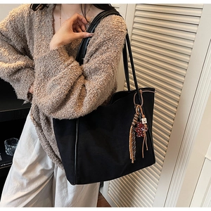 Detail of a black large tote bag with tassel charm styled with a beige knit sweater